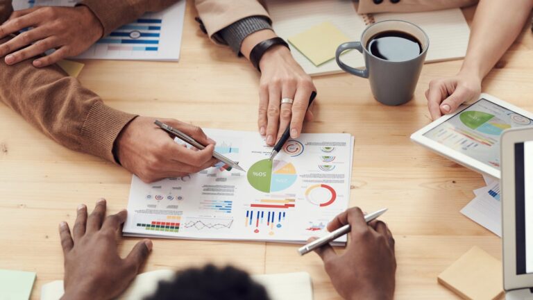 A team of employees sitting around a work table and collaborating, representing a workforce that can become a marketing engine through knowledge, insights, and tokens.