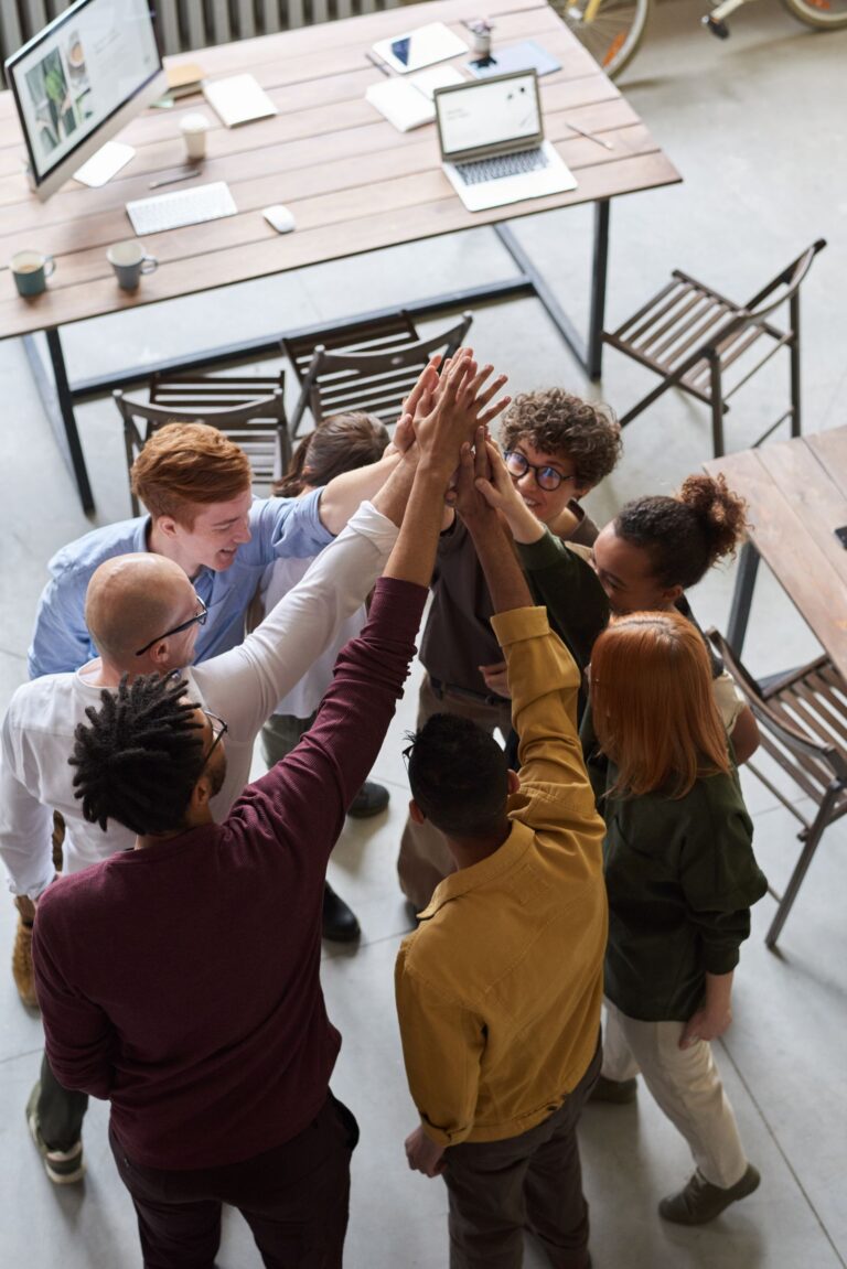 Team hands around a work table, representing community, collaboration, and belonging.