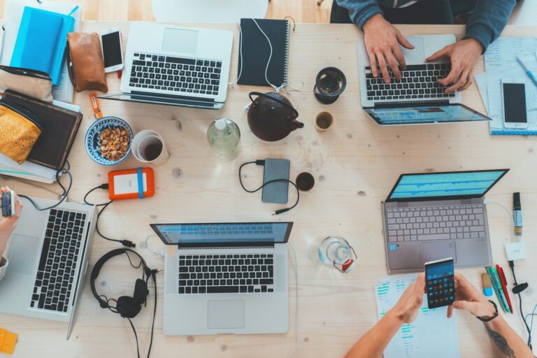 People working around a table with laptops and phones, representing digital marketing, community, and technology.