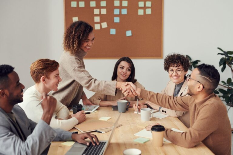 A group of people sitting around a table and collaborating, representing a community people return to through rituals, participation, and recurring value.